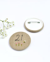 21st Birthday badge. Round badge covered in beige natural linen fabric with the number 21 sewn in black thread using freehand machine embroidery. Little flowers and a tiny bumble bee are delicately hand sewn under the embroidered number. Size 45mm. Handmade by Stitch Galore
