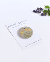 mbroidered daffodil pin badge. Four little yellow daffodil flowers and a tiny bumble bee are delicately hand sewn onto beige natural linen fabric, covering the front of the small round badge.
The round badge measures 45mm in diameter and comes attached to a branded white card.
Handmade by Stitch Galore