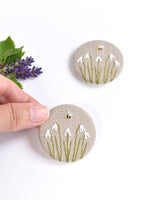 Embroidered snowdrop pin badge. Five little white snowdrop flowers and a tiny bumble bee are delicately hand sewn onto beige natural linen fabric, covering the front of the small round badge.
The round badge measures 45mm in diameter and comes attached to a branded white card.
Handmade by Stitch Galore