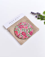 Pink Liberty fabric pocket mirror. Pretty pink floral Liberty of London fabric covers the back of the small round hand mirror.
The round pocket mirror measures 77mm in diameter and comes with a linen drawstring pouch.
Image shows the pretty pocket mirror sitting on top of the linen pouch.
Handmade by Stitch Galore.