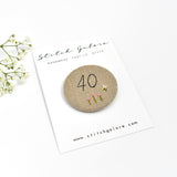 40th Birthday badge. Round badge covered in beige natural linen fabric with the number 40 sewn in black thread using freehand machine embroidery. Little flowers and a tiny bumble bee are delicately hand sewn under the embroidered number. Size 45mm. Handmade by Stitch Galore