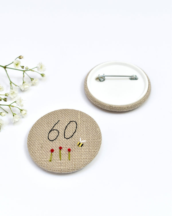18th Birthday badge. Round badge covered in beige natural linen fabric with the number 18 sewn in black thread using freehand machine embroidery. Little flowers and a tiny bumble bee are delicately hand sewn under the embroidered number. Size 45mm. Handmade by Stitch Galore