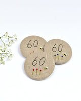 18th Birthday badge. Round badge covered in beige natural linen fabric with the number 18 sewn in black thread using freehand machine embroidery. Little flowers and a tiny bumble bee are delicately hand sewn under the embroidered number. Size 45mm. Handmade by Stitch Galore