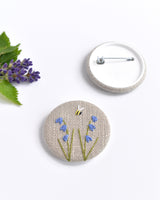 Embroidered bluebell pin badge. |Two little bluebell flowers and a tiny bumble bee are delicately hand sewn onto beige natural linen fabric, covering the front of the small round badge.
The round badge measures 45mm in diameter and comes attached to a branded white card.
Handmade by Stitch Galore
