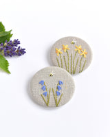 Embroidered bluebell pin badge. |Two little bluebell flowers and a tiny bumble bee are delicately hand sewn onto beige natural linen fabric, covering the front of the small round badge.
The round badge measures 45mm in diameter and comes attached to a branded white card.
Handmade by Stitch Galore