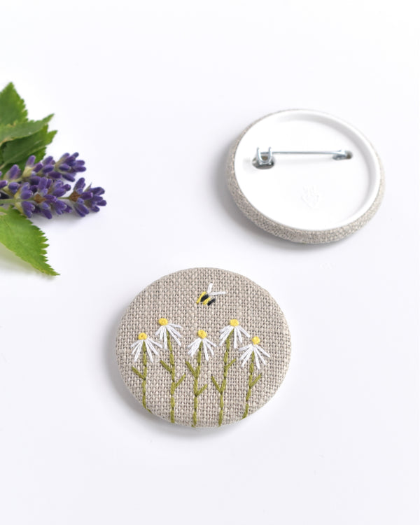 Embroidered daisy pin badge. Five little white daisy flowers and a tiny bumble bee are delicately hand sewn onto beige natural linen fabric, covering the front of the small round badge.
The round badge measures 45mm in diameter and comes attached to a branded white card.
Handmade by Stitch Galore
