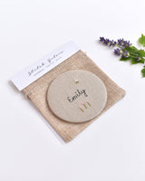 Embroidered personalised pocket mirror. An embroidered name, little flowers and a tiny bumble bee are delicately sewn onto natural linen fabric, covering the back of the small round hand mirror.
The round pocket mirror measures 77mm in diameter and comes with a linen drawstring pouch.
Image shows the pretty pocket mirror sitting on top of the linen pouch.
Handmade by Stitch Galore.

