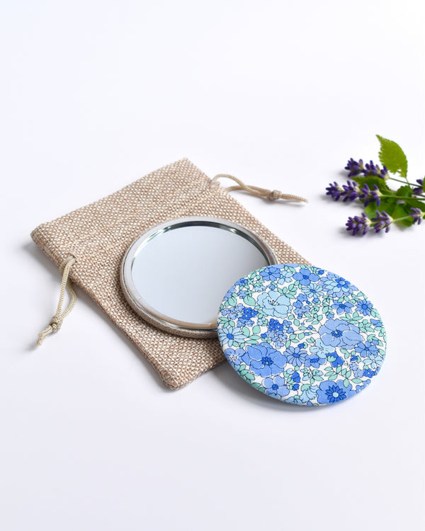 Blue Liberty fabric pocket mirror. Pretty blue floral Liberty of London fabric covers the back of the small round hand mirror.
The round pocket mirror measures 77mm in diameter and comes with a linen drawstring pouch.
Image shows the pretty pocket mirror sitting on top of the linen pouch.
Handmade by Stitch Galore.
