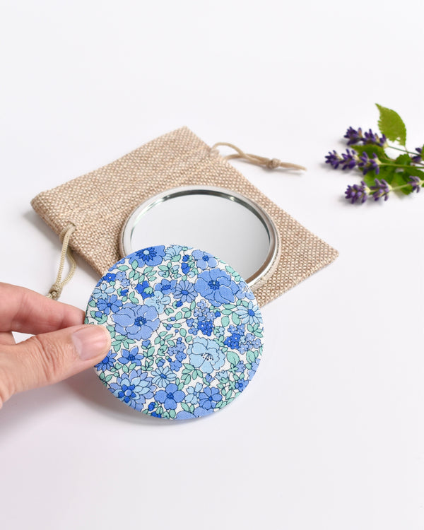 Blue Liberty fabric pocket mirror. Pretty blue floral Liberty of London fabric covers the back of the small round hand mirror.
The round pocket mirror measures 77mm in diameter and comes with a linen drawstring pouch.
Image shows the pretty pocket mirror sitting on top of the linen pouch.
Handmade by Stitch Galore.
