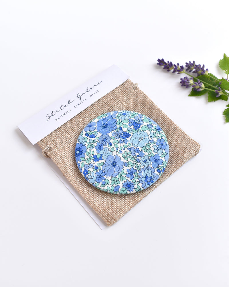 Blue Liberty fabric pocket mirror. Pretty blue floral Liberty of London fabric covers the back of the small round hand mirror.
The round pocket mirror measures 77mm in diameter and comes with a linen drawstring pouch.
Image shows the pretty pocket mirror sitting on top of the linen pouch.
Handmade by Stitch Galore.
