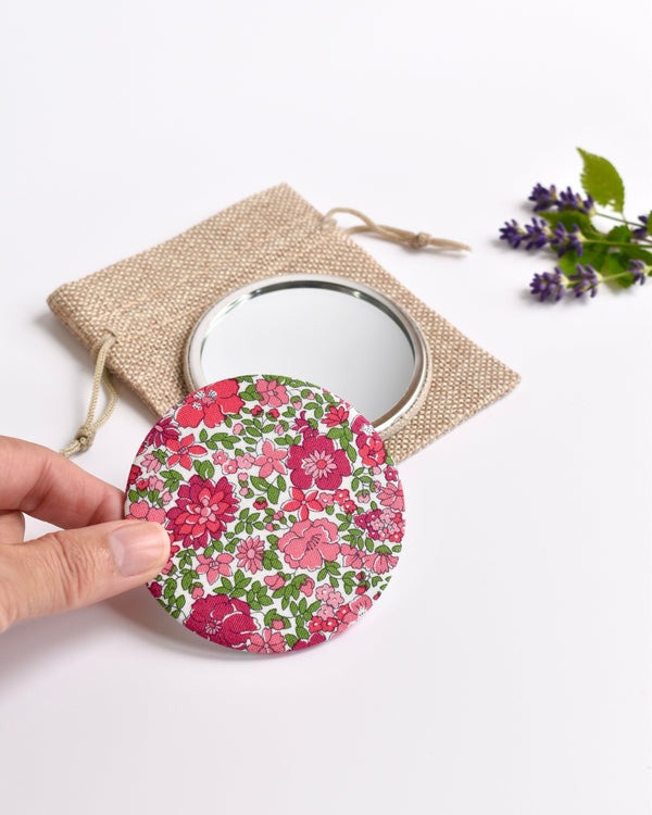 Pink Liberty fabric pocket mirror. Pretty pink floral Liberty of London fabric covers the back of the small round hand mirror.
The round pocket mirror measures 77mm in diameter and comes with a linen drawstring pouch.
Image shows the pretty pocket mirror sitting on top of the linen pouch.
Handmade by Stitch Galore.

